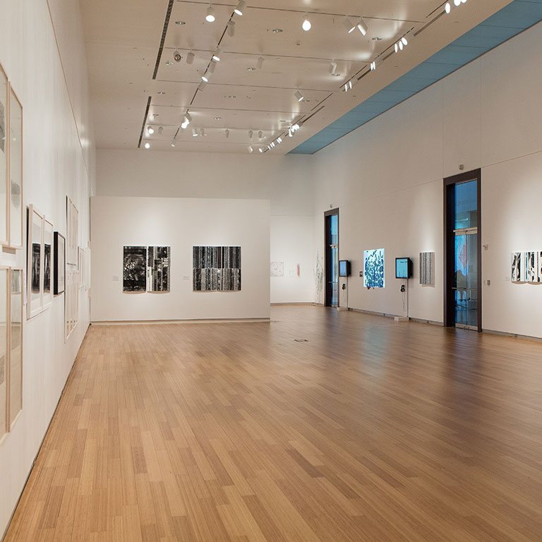 A gallery space with wood floors, tall ceilings, and plasma TVs installations on the walls.