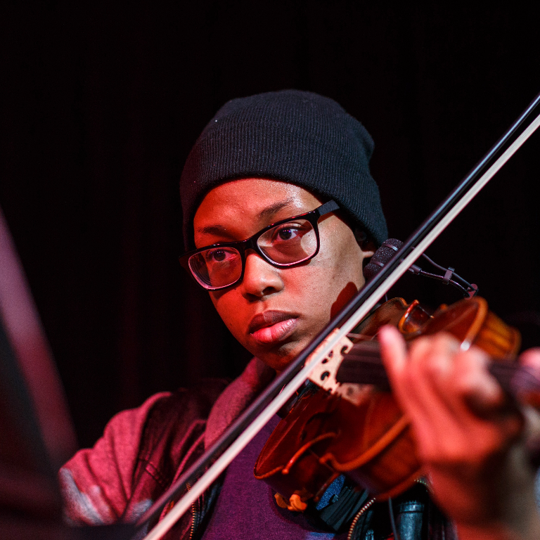 Color photograph of a Herron School of Art and Design music technology student playing violin during an ensemble performance