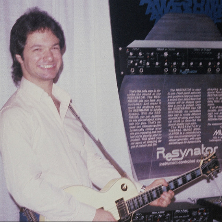 Old photograph of Donald Tavel smiling while playing guitar in front of a Resynator poster