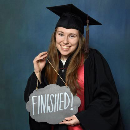 Elizah Griffith donning her graduation cap and gown while holding a sign that reads "FINISHED!"