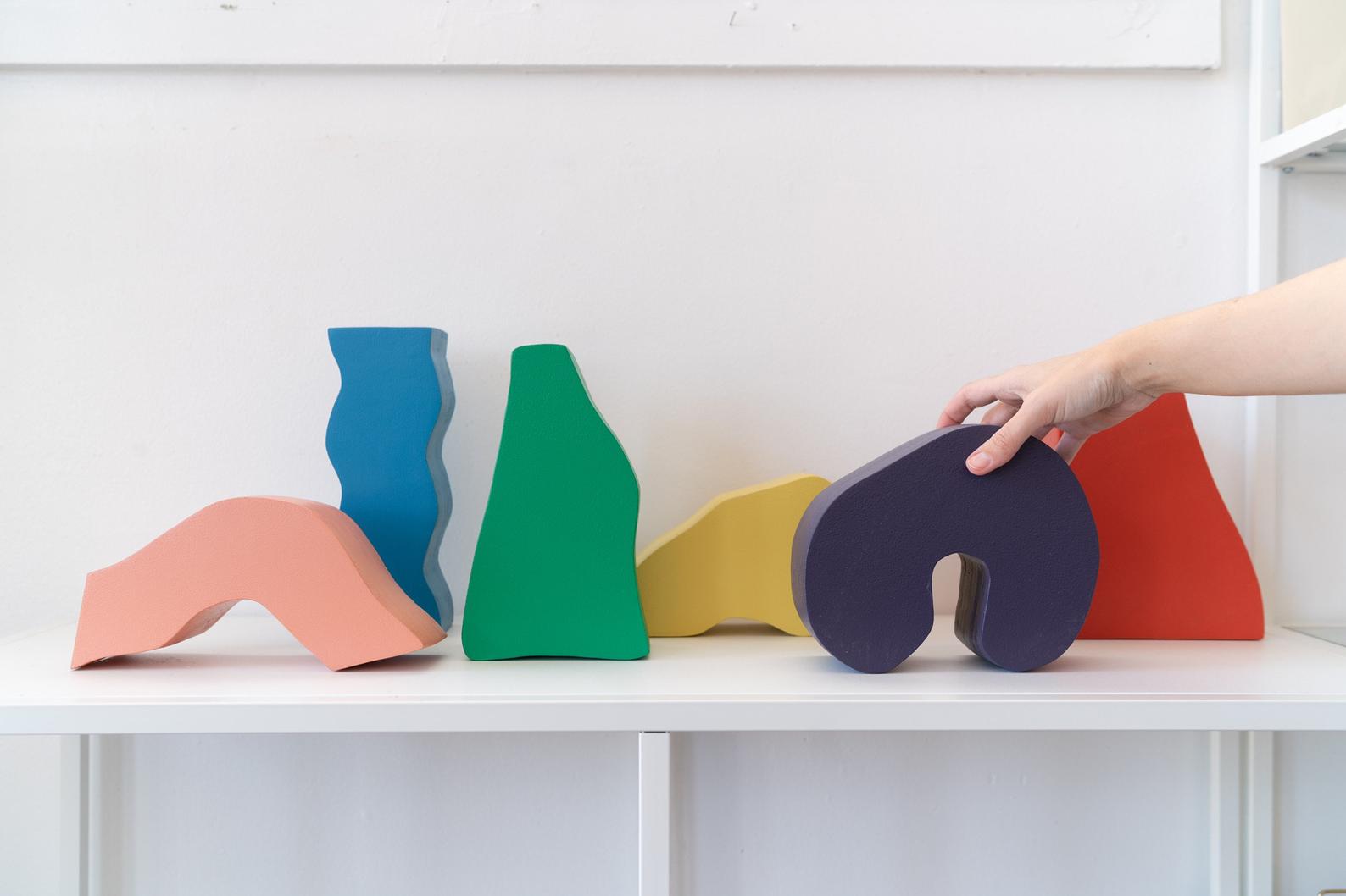 Six small sculptures in various bright colors being arranged by someone's hand