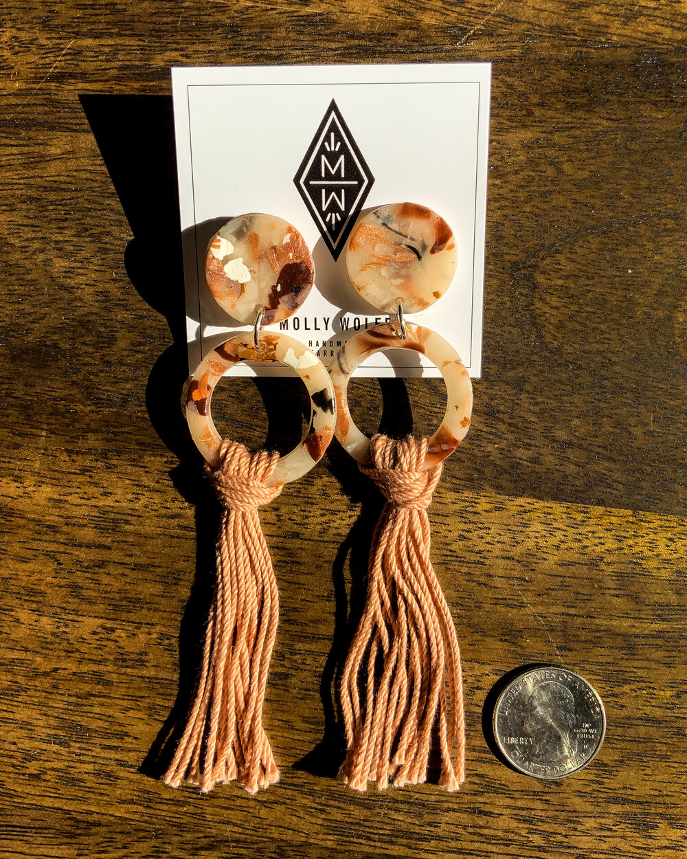 Two salmon-colored tortoise shell earrings on a display card